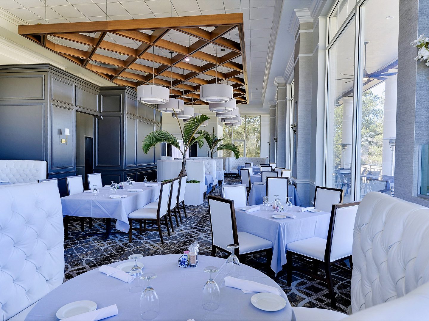 The inside of a country club with white table cloths and chairs and bright window light
