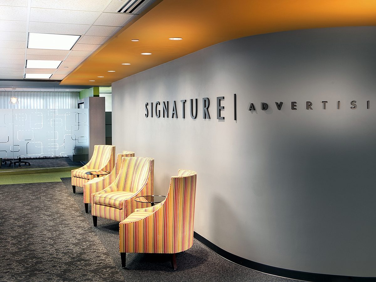 Rounded logo wall with the Signature Advertising logo on it and yellow chairs
