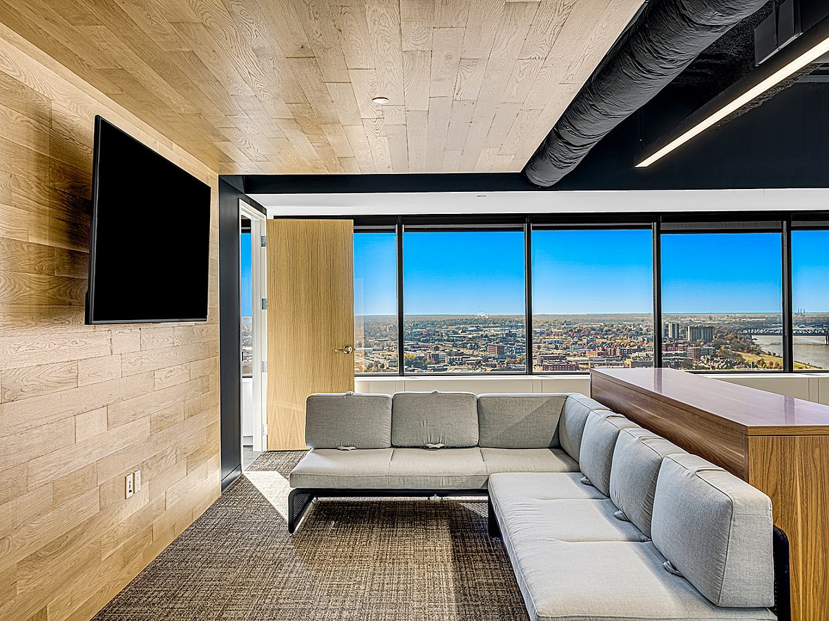 Grey couch facing a wood wall and tv with large open windows in the background