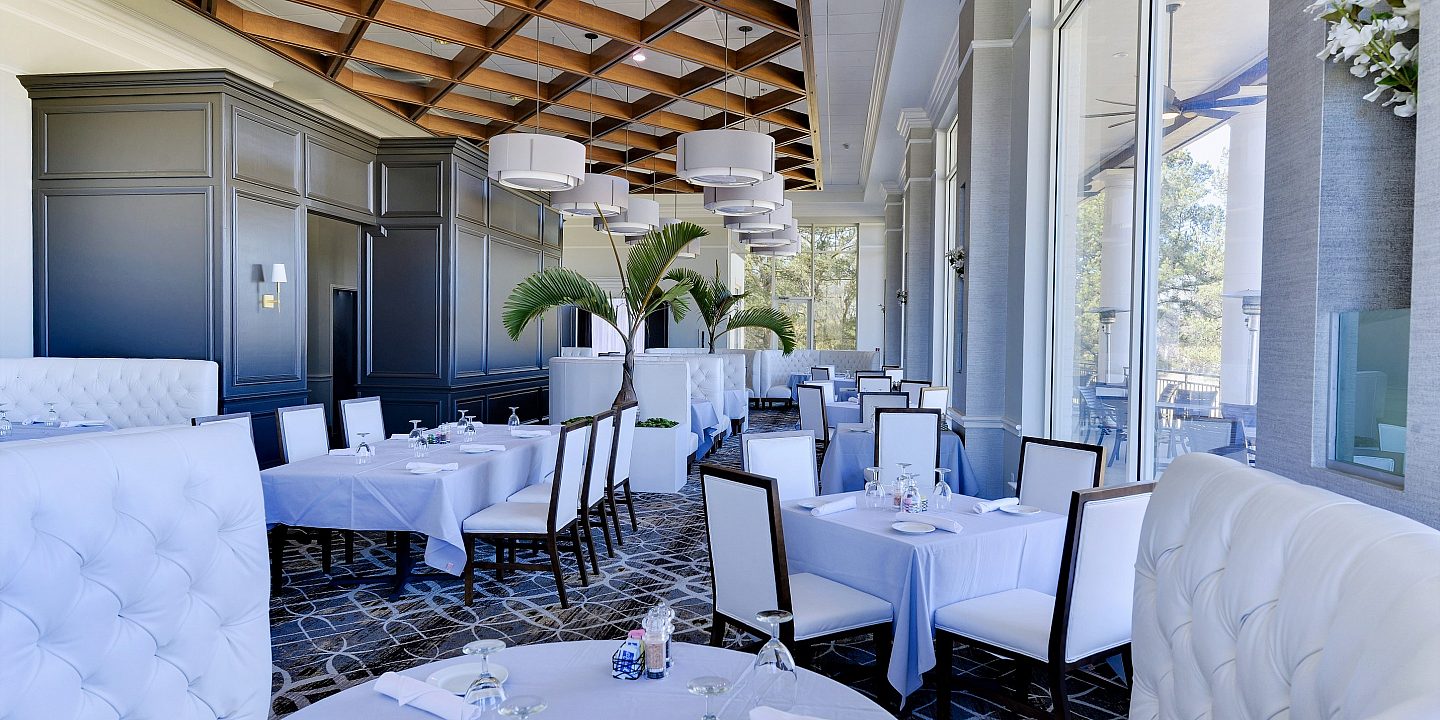 The inside of a nice restaurant with white tufted booths and white table cloths