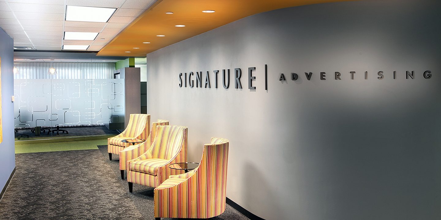Rounded logo wall with the Signature Advertising logo on it and yellow chairs