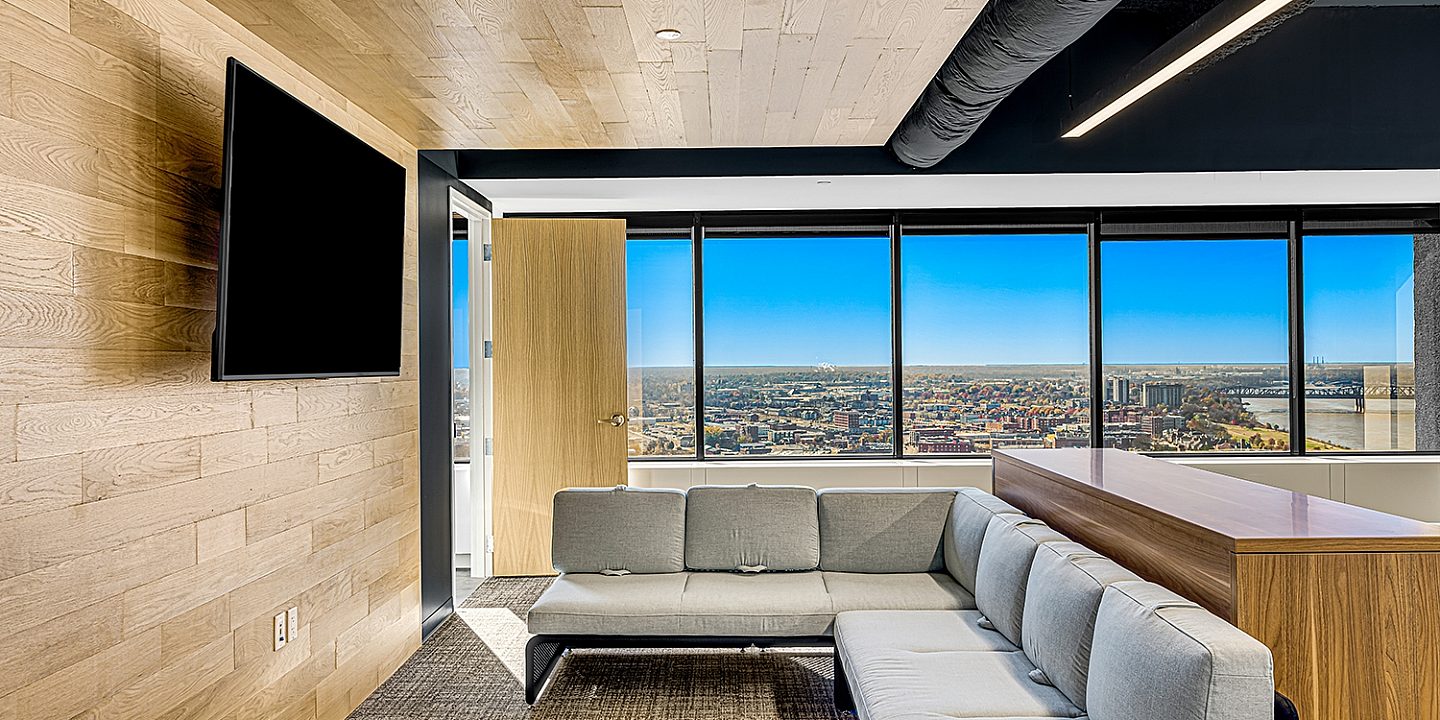 Grey couch facing a wood wall and tv with large open windows in the background